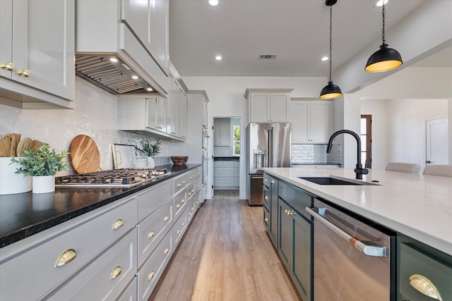 kitchen featuring light wood-style flooring, a sink, hanging light fixtures, appliances with stainless steel finishes, and dark stone countertops