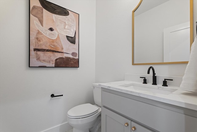 half bathroom featuring toilet, baseboards, and vanity