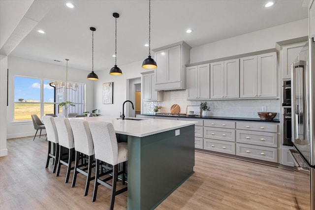 kitchen featuring decorative backsplash, a kitchen island with sink, light countertops, a kitchen bar, and pendant lighting