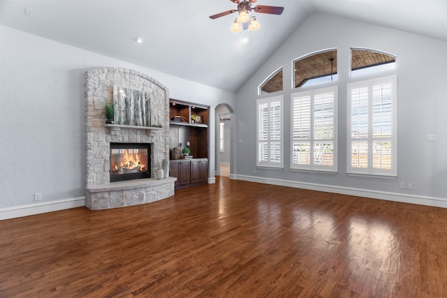 unfurnished living room featuring high vaulted ceiling, arched walkways, wood finished floors, and a stone fireplace