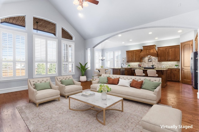 living area with arched walkways, high vaulted ceiling, wood finished floors, and baseboards