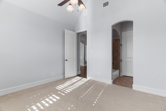 unfurnished bedroom featuring arched walkways, high vaulted ceiling, carpet flooring, visible vents, and baseboards