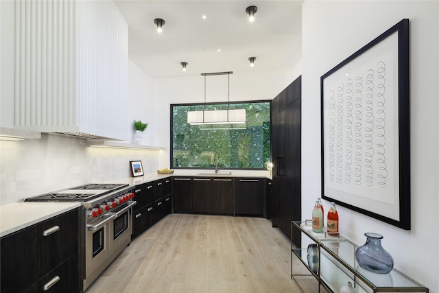 kitchen featuring range with two ovens, tasteful backsplash, light countertops, hanging light fixtures, and a sink