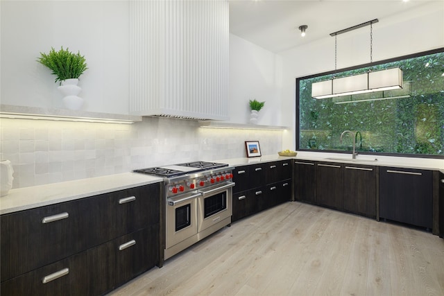 kitchen with decorative light fixtures, light countertops, light wood-type flooring, double oven range, and a sink