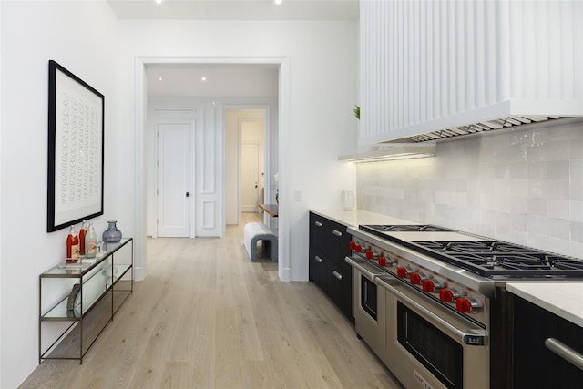 kitchen with range with two ovens, light wood-style flooring, dark cabinets, light countertops, and custom range hood