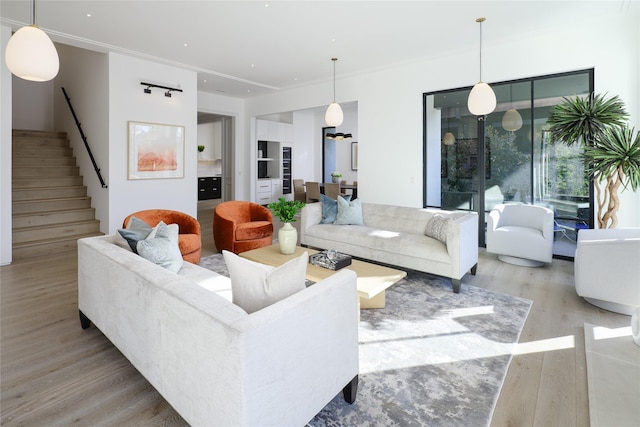 living room featuring ornamental molding, light wood-type flooring, and stairs