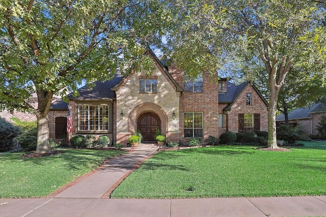 view of front of home featuring french doors, brick siding, a front lawn, and roof with shingles