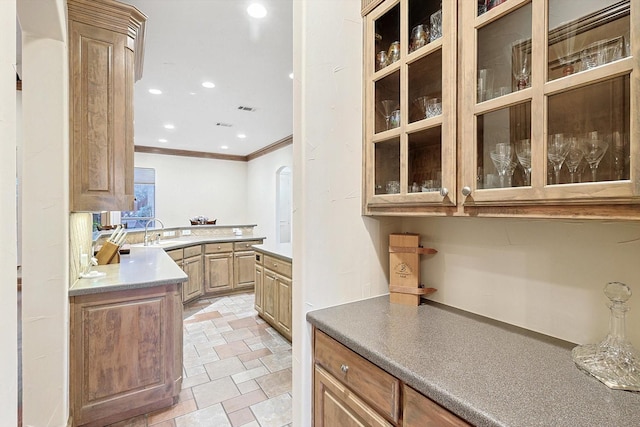 kitchen featuring light countertops, ornamental molding, a sink, and glass insert cabinets