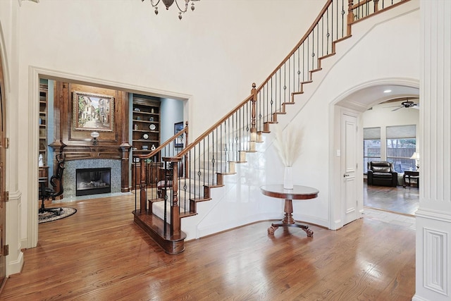 entryway with arched walkways, a towering ceiling, a premium fireplace, wood finished floors, and stairs