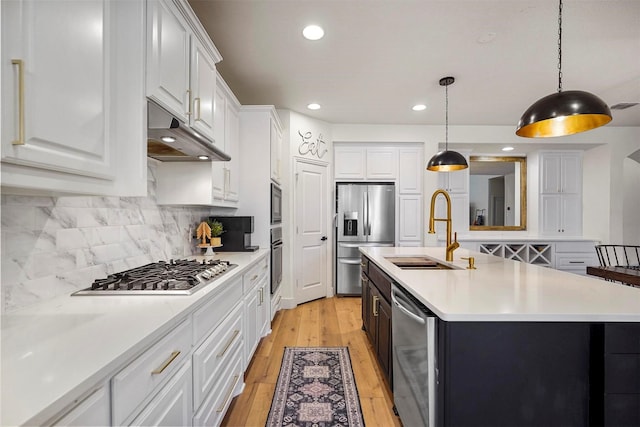 kitchen featuring light countertops, appliances with stainless steel finishes, light wood-style floors, a sink, and under cabinet range hood