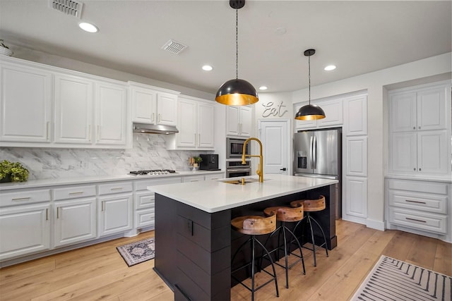 kitchen with under cabinet range hood, visible vents, stainless steel appliances, and a sink