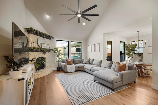 living room with a large fireplace, high vaulted ceiling, ceiling fan with notable chandelier, and wood-type flooring