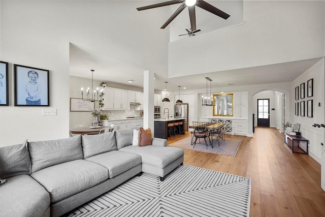 living room with arched walkways, ceiling fan with notable chandelier, a towering ceiling, and light wood-style floors