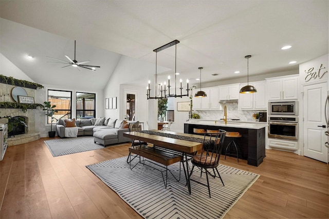 dining room with a fireplace with raised hearth, a ceiling fan, lofted ceiling, light wood-style floors, and recessed lighting