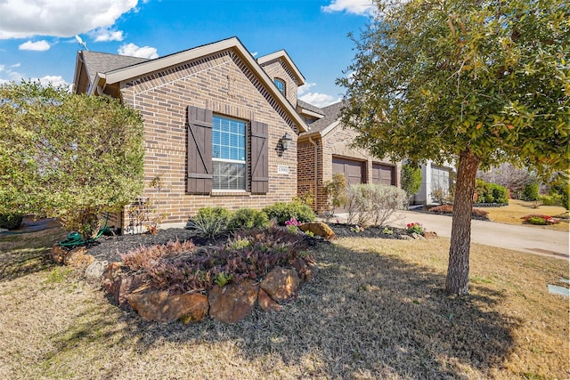 view of front of property featuring driveway, brick siding, a front lawn, and an attached garage