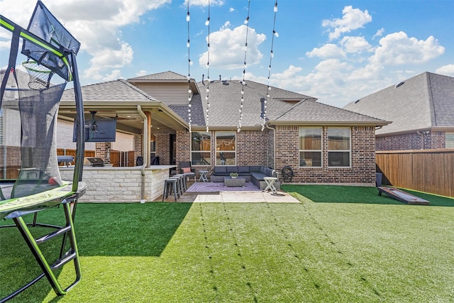 rear view of property with a trampoline, a yard, a patio area, an outdoor living space, and brick siding