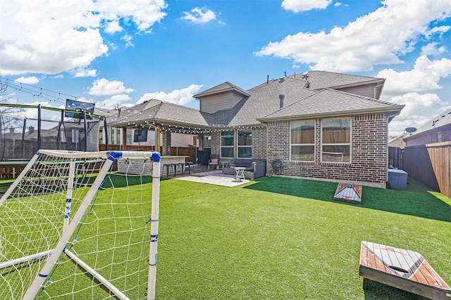 back of property with a fenced backyard, brick siding, roof with shingles, a trampoline, and a patio area