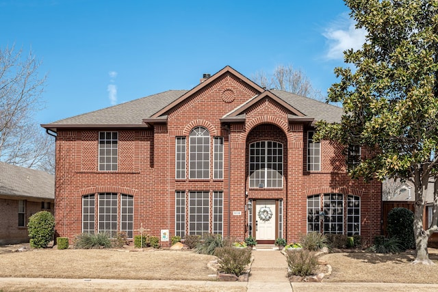 view of front of home featuring roof with shingles, a chimney, and brick siding