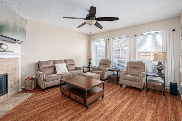 living area featuring a ceiling fan, a textured ceiling, a tiled fireplace, and wood finished floors