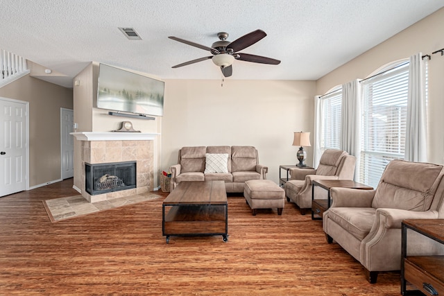 living room featuring ceiling fan, a fireplace, visible vents, and wood finished floors