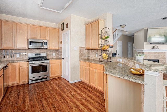 kitchen featuring tasteful backsplash, appliances with stainless steel finishes, dark wood-type flooring, a peninsula, and light brown cabinetry