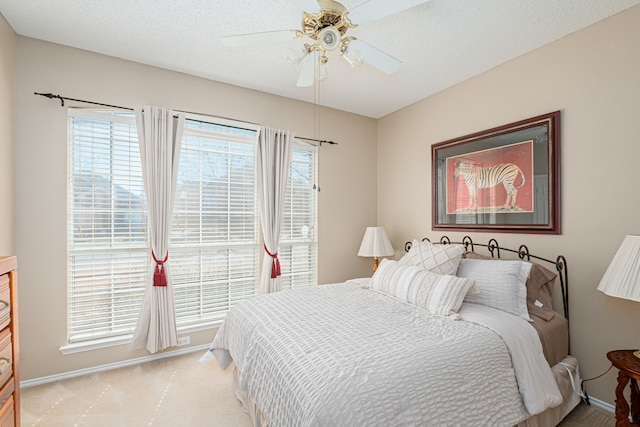 bedroom featuring a ceiling fan, light carpet, a textured ceiling, and baseboards