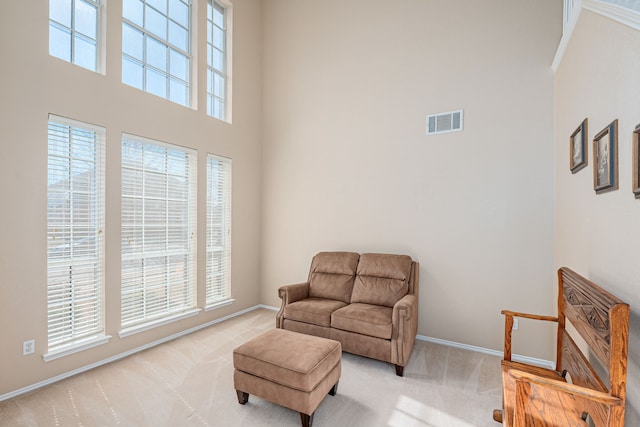 living area featuring light carpet, a towering ceiling, visible vents, and a wealth of natural light