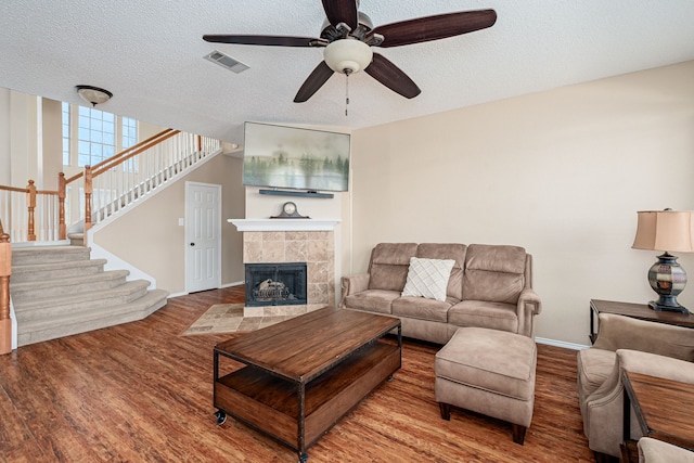 living area with visible vents, a tile fireplace, stairway, wood finished floors, and a textured ceiling