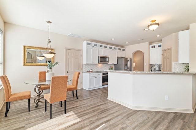 kitchen featuring light wood finished floors, visible vents, white cabinets, arched walkways, and appliances with stainless steel finishes