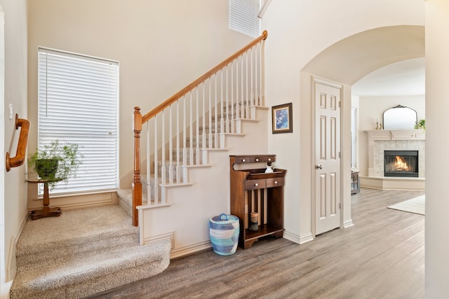 stairs with baseboards, a fireplace, arched walkways, and wood finished floors