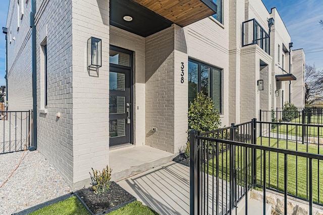 view of exterior entry with brick siding, a lawn, and fence