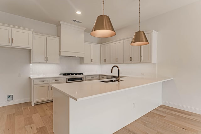 kitchen with a sink, white cabinetry, light countertops, hanging light fixtures, and light wood-type flooring