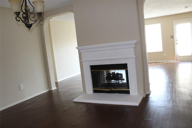 unfurnished living room featuring dark wood-style floors, arched walkways, baseboards, and a multi sided fireplace