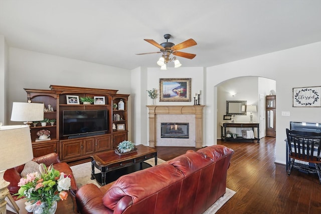 living room with ceiling fan, arched walkways, dark wood-style flooring, and a glass covered fireplace