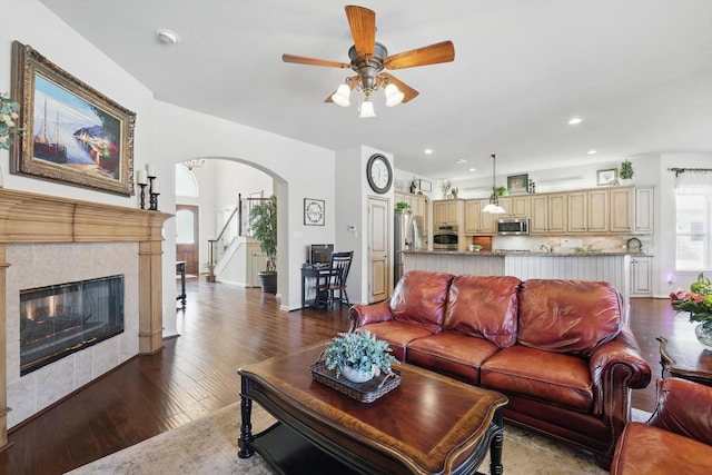 living room with arched walkways, dark wood finished floors, recessed lighting, ceiling fan, and a tile fireplace