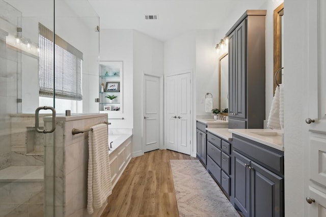 full bathroom featuring double vanity, a stall shower, visible vents, wood finished floors, and a garden tub