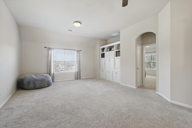 unfurnished bedroom with arched walkways, light colored carpet, a ceiling fan, baseboards, and visible vents