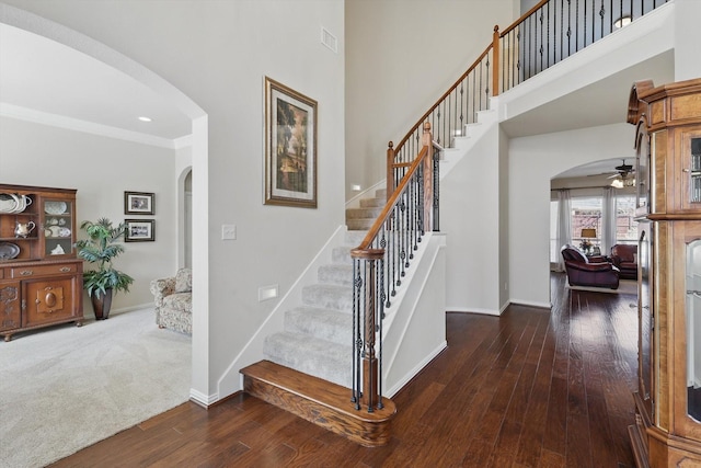 stairway with a towering ceiling, baseboards, arched walkways, and hardwood / wood-style floors