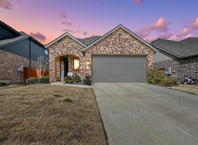 view of front of house with an attached garage, brick siding, fence, concrete driveway, and a front lawn