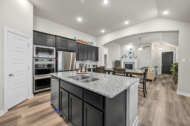 kitchen featuring a center island with sink, appliances with stainless steel finishes, open floor plan, dark cabinetry, and a sink