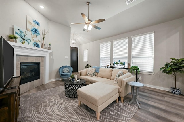 living room with baseboards, a ceiling fan, a tiled fireplace, lofted ceiling, and wood finished floors