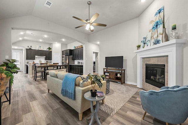 living room with vaulted ceiling, a tile fireplace, dark wood finished floors, and visible vents