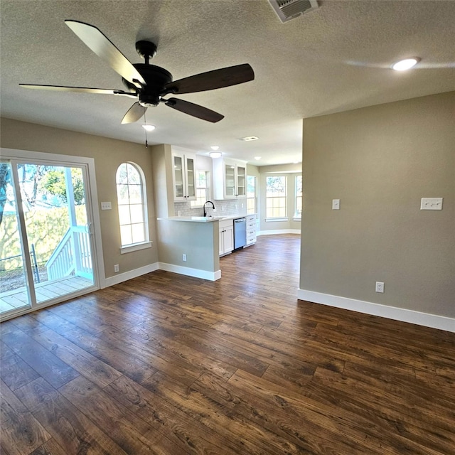 unfurnished living room featuring visible vents, dark wood-type flooring, a sink, a textured ceiling, and baseboards