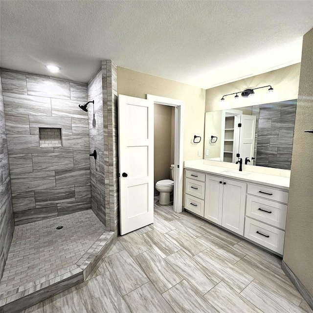 bathroom featuring tiled shower, vanity, toilet, and a textured ceiling