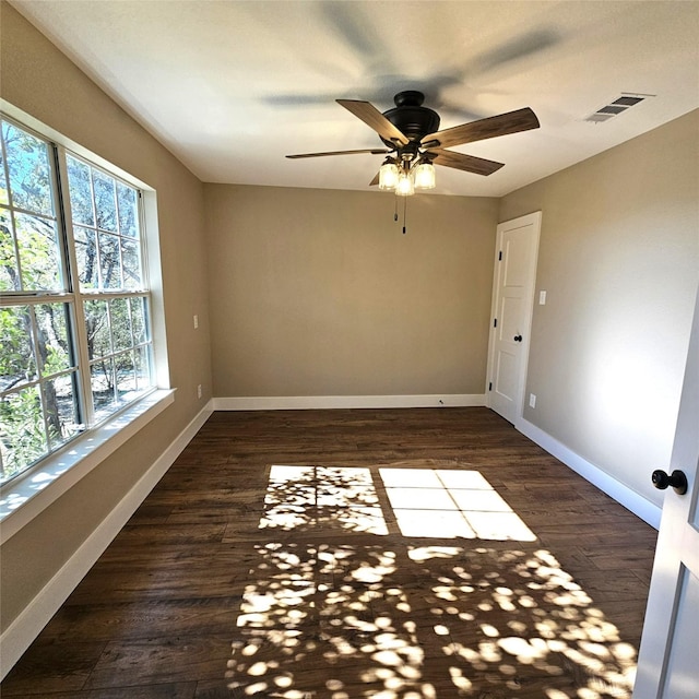 empty room with dark wood-style floors, baseboards, visible vents, and ceiling fan