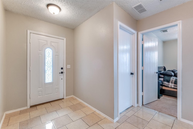 foyer entrance featuring light tile patterned floors, a textured ceiling, visible vents, and baseboards