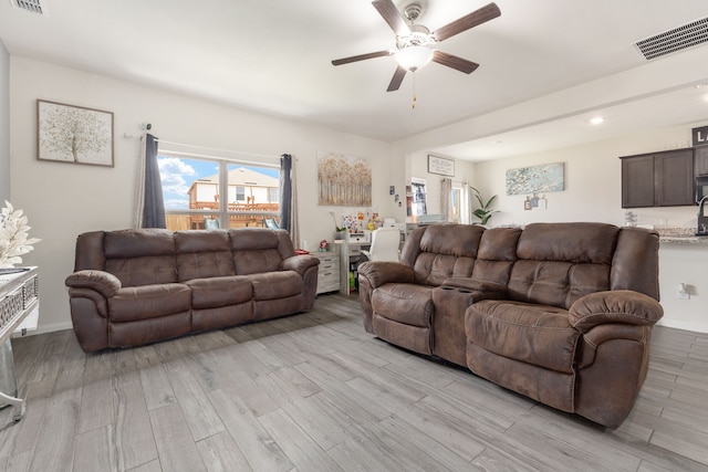 living area featuring light wood-style floors, visible vents, baseboards, and a ceiling fan