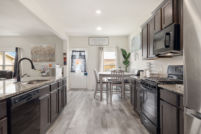 kitchen with light wood finished floors, a sink, dark brown cabinets, light stone countertops, and black appliances