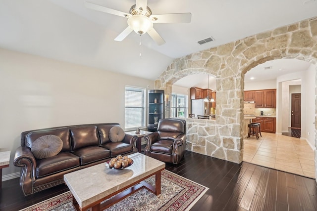 living area with arched walkways, visible vents, lofted ceiling, and hardwood / wood-style flooring