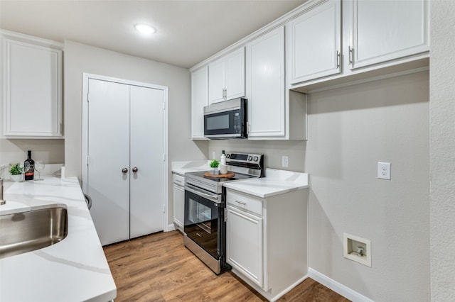 kitchen with light wood-style flooring, appliances with stainless steel finishes, white cabinets, a sink, and baseboards